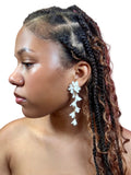 Woman with braided hair wearing white floral earrings against a white background