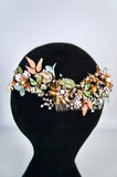 Floral headpiece with green and gold elements on a black mannequin head against a light gray background