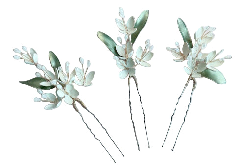 A set of three ivory enamel hair pins with floral details and green leaves, on a light background.